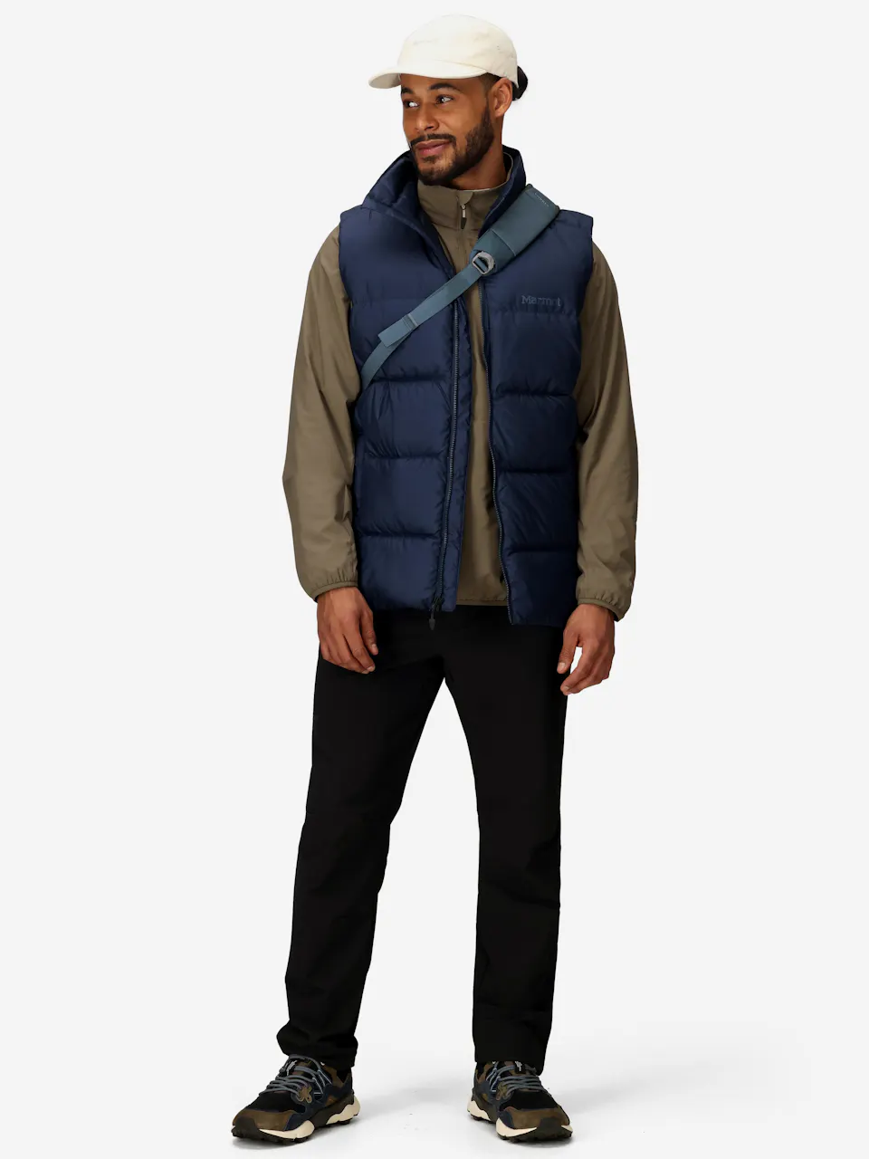 Man wearing a blue puffer vest, casual long sleeve shirt, black pants, sneakers, and a crossbody bag