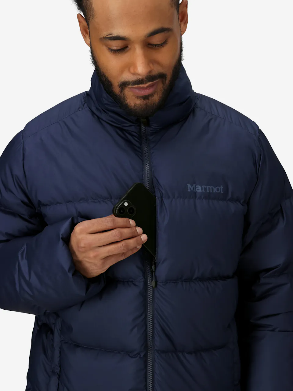 Man wearing a warm blue puffer jacket with front zipper, holding a black smartphone in chest pocket.