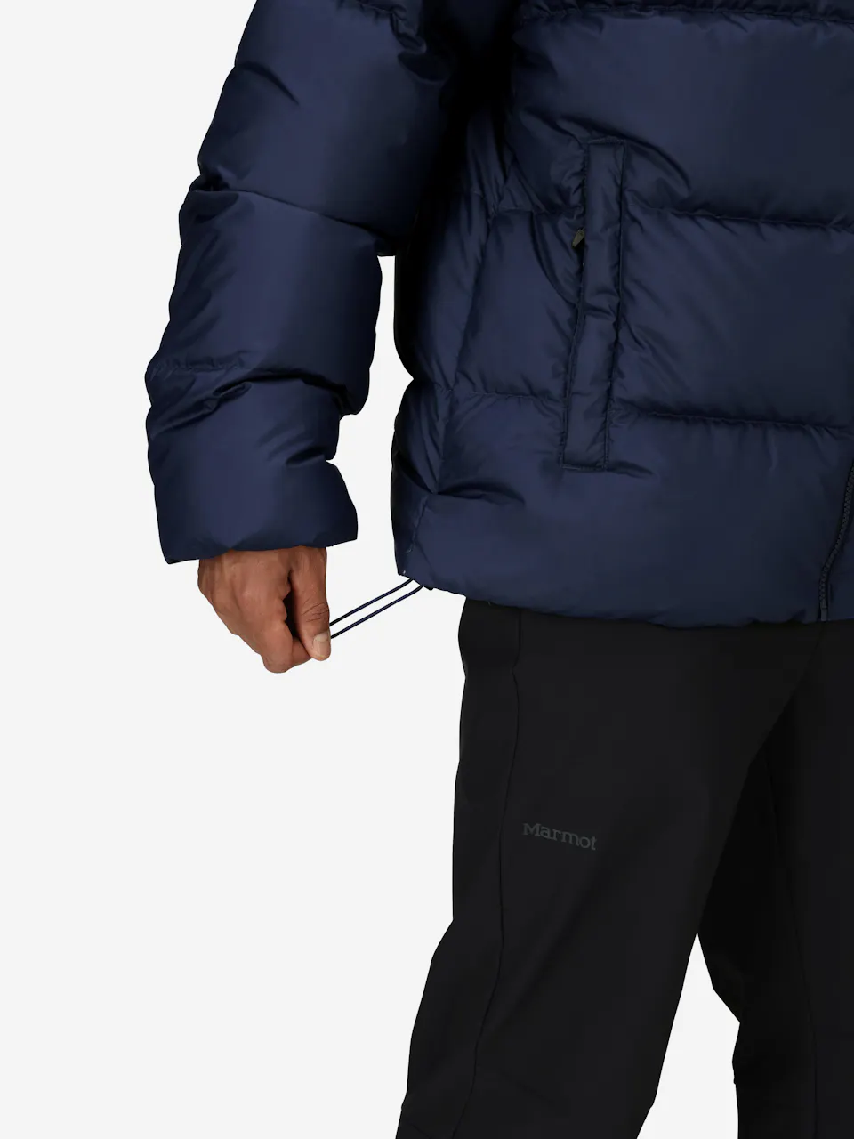 Man adjusts blue puffer jacket with drawstring, wearing black pants, showing insulated winter outerwear style